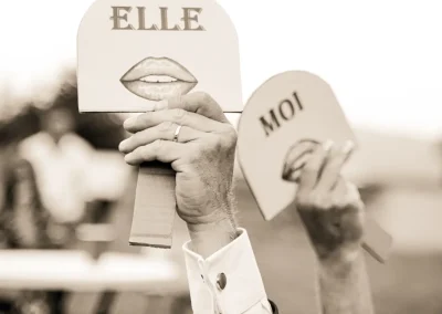 Détail émouvant : Deux mains amoureuses se tiennent délicatement l'une contre l'autre, capturées en noir et blanc avec des pancartes d'amour en arrière-plan